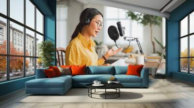 Asian woman recording a podcast on laptop computer with microphone while online live streaming at home Wall mural