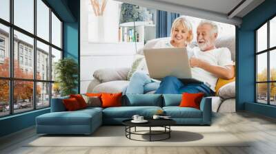 Couple senior using computer laptop on sofa at home for online shopping, surfing internet Wall mural