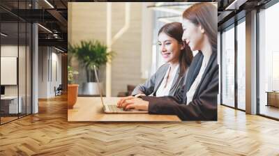 Two Asian businesswoman in suit happy working with laptop at modern office Wall mural