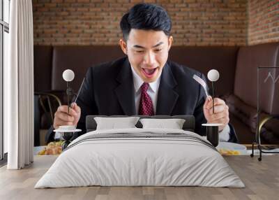 Young asian businessman in formal suit feeling hungry, eating many foods on table at cafe Wall mural