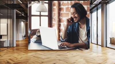 Young Asian man talking on phone and working on laptop for business creative designer Wall mural