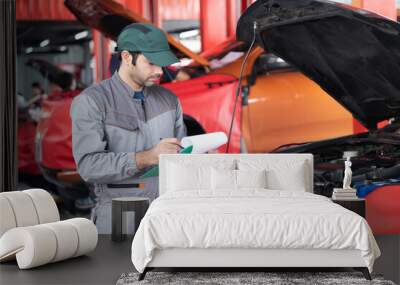 car service, repair, maintenance concept - Arab auto mechanic man or Smith writing to the clipboard at workshop warehouse, technician doing the checklist for repair machine a car in the garage Wall mural