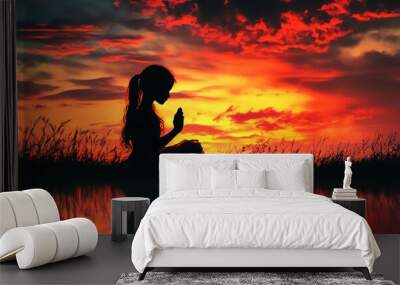 Prayer concept with girl child silhouette in a praying pose, vibrant sunset or sunrise sky, clasped hands, holistic union, and reflection Wall mural