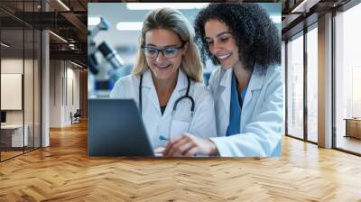 Two diverse female scientists smiling while working together on laptop in laboratory, showcasing collaboration and innovation in science Wall mural