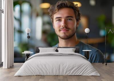 A young man with a beard and curly hair smiles confidently at the camera, in a modern cafÃ© with soft, natural lighting perfect for lifestyle, business, or social media content, Wall mural