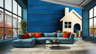 Wooden house model with coins on blue wooden background, representing real estate value. Wall mural