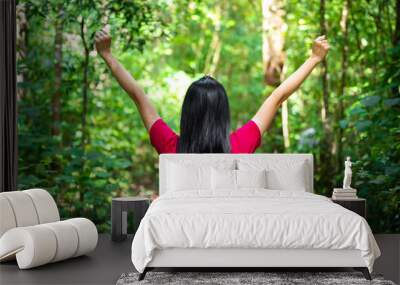 A girl in red shirt is lifting up her arm for relaxing, with background of tropical greenery jungle. Relaxation in the natural concept photo. Wall mural