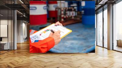 A worker is checking on the hazardous chemical material information form with background of chemical storage area at the factory place. Industrial safety working action. Selective focus. Wall mural