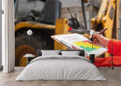 The operation supervisor is using ballpoint pen to marking on the risk assessment matrix form, to inspection the backhoe machine that using at construction worksite. Wall mural