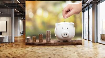 Hands putting coins on a piggy bank with a natural blur background. a pile of coins, business, investment, finance, and Money Saving for the future concepts Wall mural