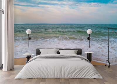 Curving tropical sea waves on the beach. White clouds on the soft blue sky in the background. Wall mural