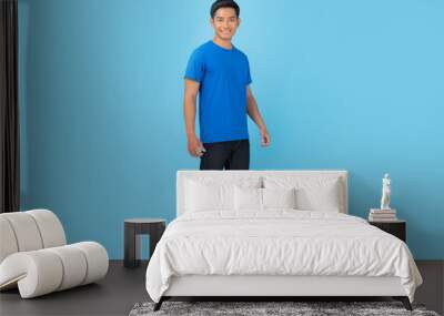 Young man in blue t-shirt isolated on blue background Wall mural