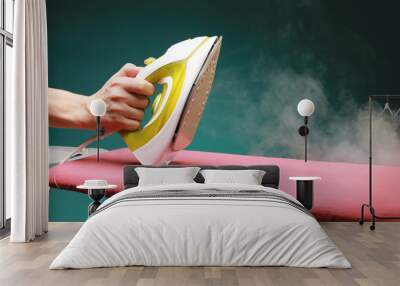 male hand holds the  modern electric iron from which steam is coming on ironing board isolated on green background Wall mural