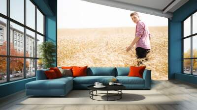 Courageous handsome guy standing in a field among wheat. Summer is the time to harvest Wall mural