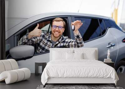 Excited young man showing a car key, sitting inside his new vehicle Wall mural