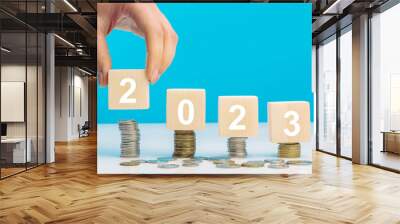 Hand place wooden cube 2023 with stack of coins with blue background and copy space. Saving money and financial plan concept for investment in new year 2023. Wall mural