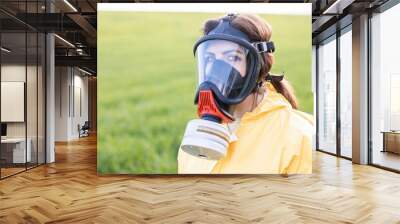 person in overalls and gas mask call to save the planet while standing on green field on sunset. con Wall mural