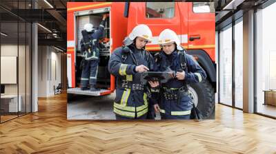 Portrait of two firefighters in fire fighting operation, fireman in protective clothing and helmet using tablet computer in action fighting. Wall mural