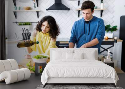 Young cute smiling couple cooking together at kitchen at home. Young people are preparing a salad in a good kitchen Wall mural