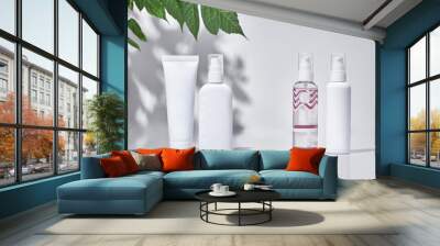 Cosmetic tube and three pump bottles with no logo standing on surface against white studio background and green branch. Close up, copy space Wall mural