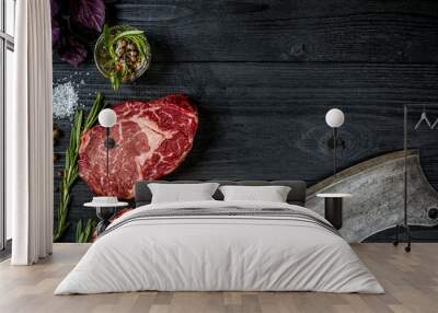 Fresh raw beef with basil and a sprig of rosemary with ax for meat on black wooden background. Top view Wall mural