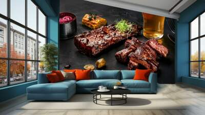 Pork ribs in barbecue sauce and a glass of beer on a black slate dish. A great snack to beer on a dark stone background. Top view with copy space Wall mural