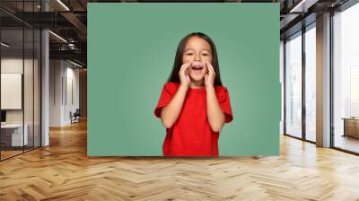 Portrait of a small pretty girl standing sideways and calling someone holding her hand near her mouth Wall mural