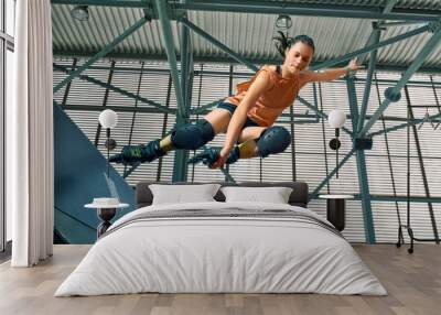 Rollerblader jump high from big air ramp performing trick. Indoors skate park equipment. Wall mural