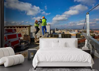 Two workers in protective clothing and safety helmets are working with ventilation system on roof of building under construction Wall mural