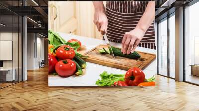 Young woman cooking in the kitchen at home. A woman cuts a cucumber and vegetables with a knife. Wall mural