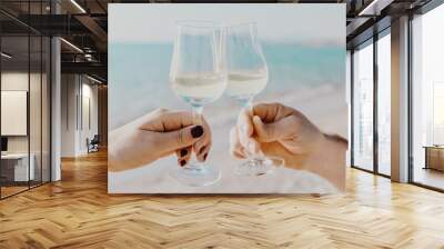 Two hands holding glasses with white wine on sea background in Italy. Wall mural