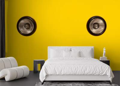 Two black headlights. Yellow background. Wall mural