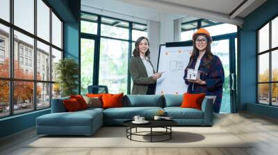 Concept of engineering consulting, Two female engineers discussing about model of building together; Two female architects are studying blueprint of building house. Wall mural