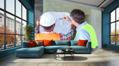 Two construction engineers holding blue print and inspecting the construction site Wall mural