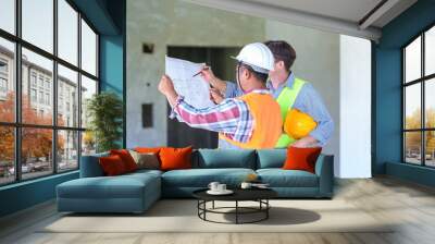 Two construction engineers holding blue print and inspecting the construction site Wall mural