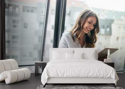 attractive businesswoman using a digital tablet while standing in front of windows Wall mural