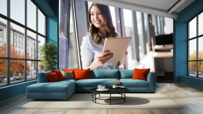 Attractive businesswoman using a digital tablet while standing in front of windows Wall mural