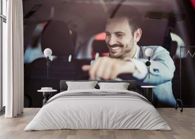 Attractive happy young man driving car and smiling Wall mural