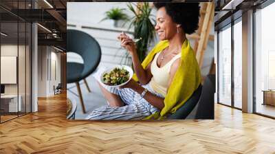 Beautiful afro american woman eating vegetable salad at home. Wall mural