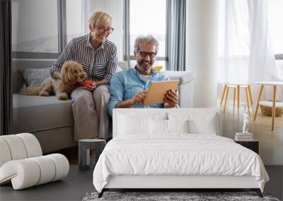 Beautiful happy mature couple is using a digital tablet, talking and smiling at home Wall mural