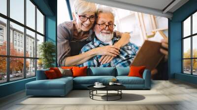 Beautiful old couple is reading a book and smiling at home Wall mural