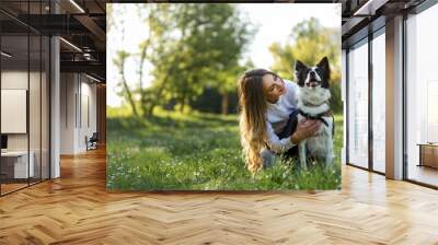 Beautiful woman with playful dog on fresh green meadow Wall mural