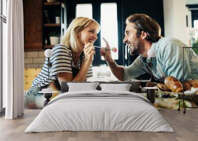 Beautiful young couple is smiling while cooking together in kitchen at home Wall mural