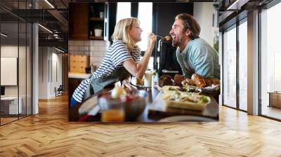 Beautiful young couple is smiling while cooking together in kitchen at home Wall mural