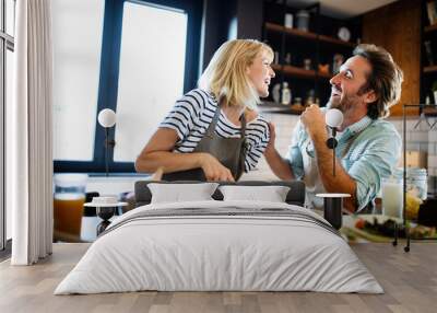 Beautiful young couple is talking and smiling while cooking healthy food in kitchen at home Wall mural