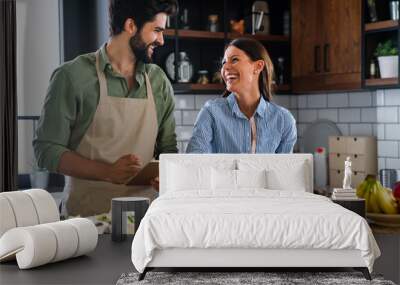 Beautiful young couple is using a digital tablet and smiling while cooking in kitchen at home Wall mural