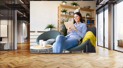 Cheerful young woman resting with tablet computer at home Wall mural