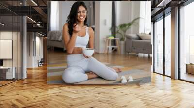 Fit woman eating healthy salad after working out at home Wall mural