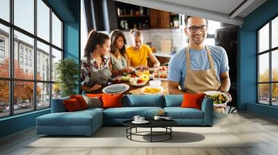 Group of happy friends laughing and talking while preparing meals in kitchen Wall mural