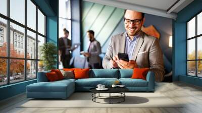 Handsome businessman checking emails on the phone in modern office Wall mural